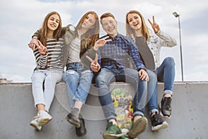 Group of smiling teenagers with skateboard hanging out outside.