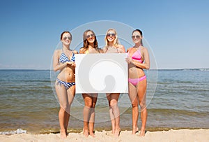 Group of smiling women with blank board on beach