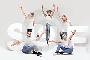 Group of smiling young people posing with sale letters.