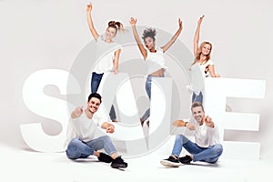 Group of smiling young people posing with sale letters.