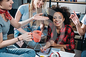 Group of smiling young women drinking coffee and studying together