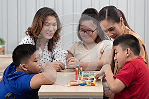 Group of special students in classroom, a down syndrome girl, two handicapped boys and cute Asian teacher playing toy and game