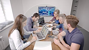 Group of specialists are working in office room, sitting at one large table, having coffee break