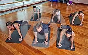 A group of sporting young people in sportswear, in a fitness room, doing push-ups or planks in the gym. Group fitness