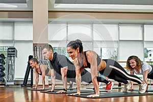 A group of sporting young people in sportswear, in a fitness room, doing push-ups or planks in the gym. Group fitness