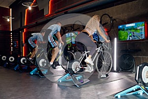 Group of sports people riding stationary bike at gym