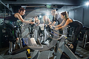 Group of sporty girl exercising together on indoor bikes at cycling class in the gym