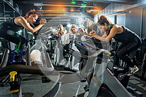 Group of sporty girls riding exercise bikes together on cycling training at gym