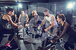 Group of sporty people with personal trainer exercising together during cycling class in gym