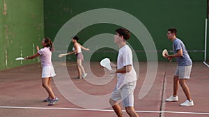 Group of sporty young people in sportswear playing paleta fronton on outdoor court