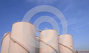 Group of storage fuel tanks with oil pipeline system in petroleum industrial area against blue sky background