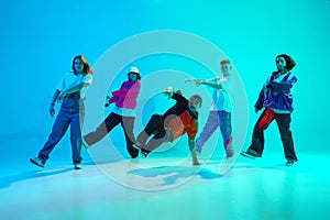 Group of streetstyle dancers energetically moves in sync in neon light against gradient colorful studio background.