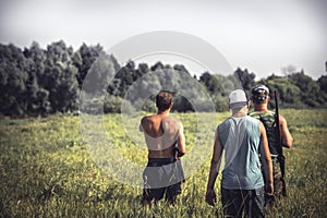 Group of strong male hunters going through rural field with tall grass during hunting season