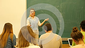 Group of students attentively listening to lecture of female teacher in classroom