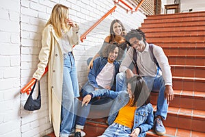 Group of students with ethnic variety, sitting on some street steps having fun together.