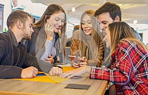 Group of students hangging out with each other sitting in a bar - Friends checking out social media and looking in a smartphone photo