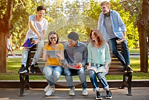 Group Of Students Relaxing Sitting On Bench In Park Outside