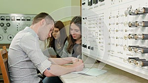 A group of students working together on a test bench Physical Laboratory. Many switches and lights. Men and women write