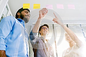 Group of successful Asian businessmen teamwork. Brainstorm meeting with sticky paper notes on the glass wall for new ideas.