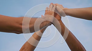 A group of successful people raise their hands up and hold hands against the blue sky, together they are a successful