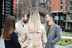 Group of successful young business people, leaders in marketing and motivation, stand in front of office building and consult