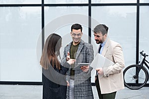 Group of successful young business people, leaders in marketing and motivation, stand in front of office building and consult