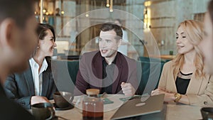 Group of suit wearing colleagues discussing working situation sitting at table in cafe with laptop. Casual coworkers