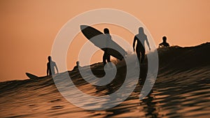 A group of surfers riding waves in silhouette at sunset, AI
