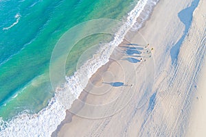 a group of surfers walking with their surfboards under their arms along the shore of a beach, aerial drone view