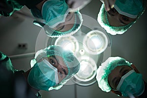 Group of surgeons doing surgery in hospital in the modern operating room under lights. Doctor and nurse wear protective suit and