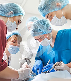 Group of surgeons at work operating in surgical theatre. Resuscitation medicine team wearing protective masks holding