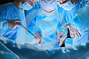 Group of surgeons at work in operating theater toned in blue