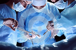 Group of surgeons at work in operating theater toned in blue