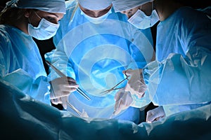 Group of surgeons at work in operating theater toned in blue