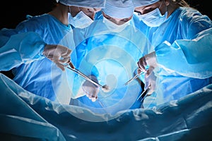 Group of surgeons at work in operating theater toned in blue