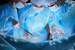 Group of surgeons at work in operating theater toned in blue