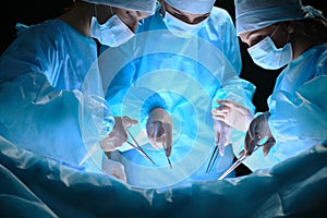 Group of surgeons at work in operating theater toned in blue