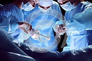 Group of surgeons at work in operating theater toned in blue