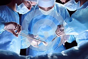 Group of surgeons at work in operating theater toned in blue