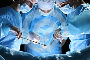 Group of surgeons at work in operating theater toned in blue