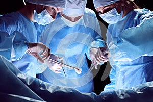 Group of surgeons at work in operating theater toned in blue