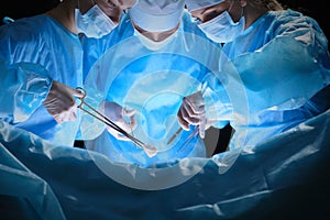 Group of surgeons at work in operating theater toned in blue