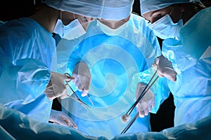 Group of surgeons at work in operating theater toned in blue