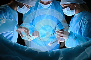 Group of surgeons at work in operating theater toned in blue