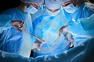 Group of surgeons at work in operating theater toned in blue