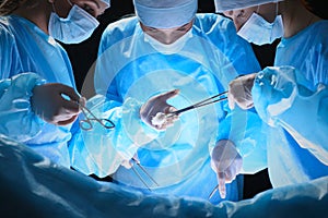 Group of surgeons at work in operating theater toned in blue