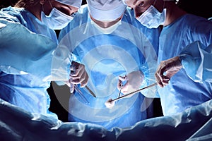 Group of surgeons at work in operating theater toned in blue