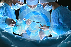 Group of surgeons at work in operating theater toned in blue