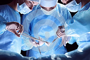 Group of surgeons at work in operating theater toned in blue