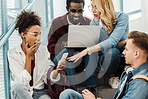 Group of surprised multicultural students with laptop and smartphone